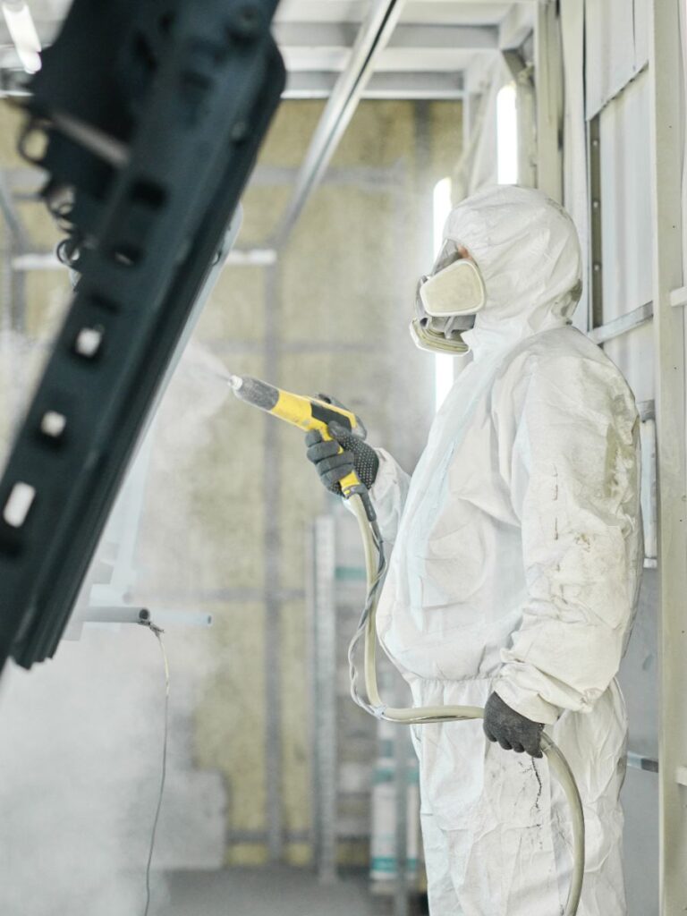 Medewerker in beschermende kleding brengt een poedercoating aan op metalen onderdelen in een professionele spuitcabine