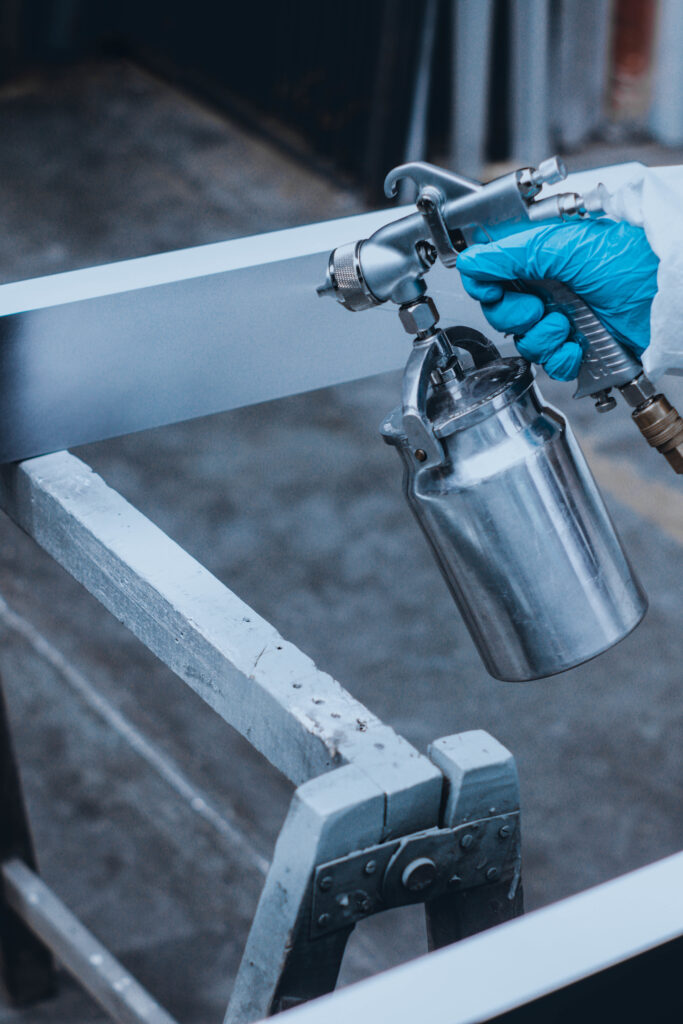 Close-up van een spuitpistool dat een metalen frame voorziet van een egale beschermende coating